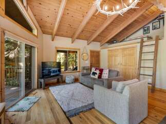 Experience rustic charm in this cozy living room featuring a vaulted wood-paneled ceiling with exposed beams and a unique antler chandelier.