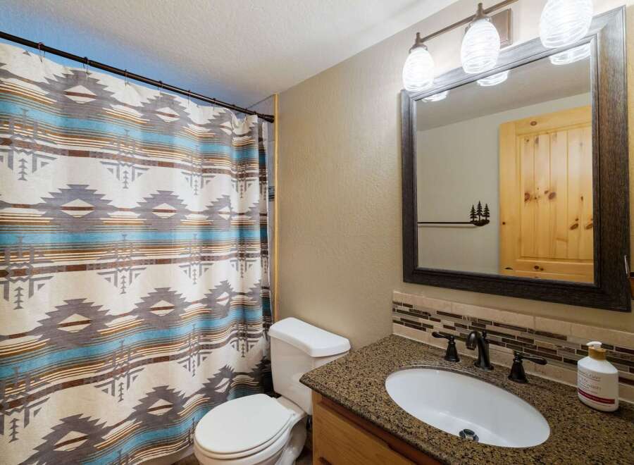 This bathroom features a stylish shower curtain with a Native American-inspired pattern, complementing the granite countertop and wooden vanity.
