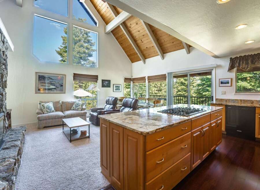 Experience breathtaking views from this stunning living space, featuring a grand stone fireplace and soaring vaulted ceilings with exposed wooden beams.