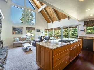 Experience breathtaking views from this stunning living space, featuring a grand stone fireplace and soaring vaulted ceilings with exposed wooden beams.