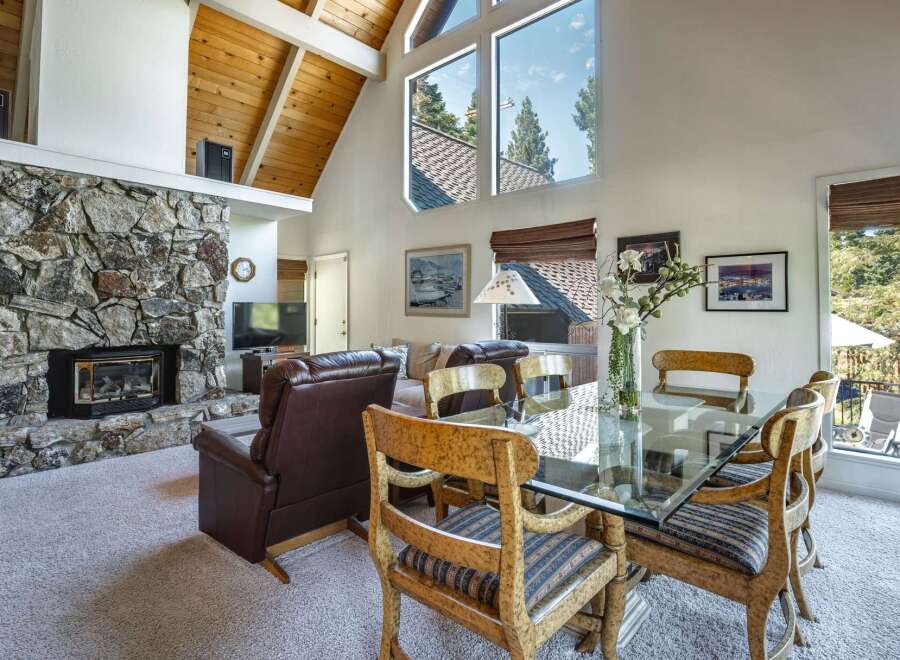 Experience breathtaking mountain views from this stunning living and dining area, featuring a grand stone fireplace and vaulted wood-beamed ceilings.