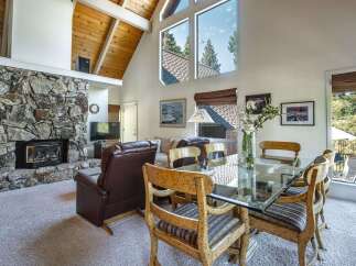 Experience breathtaking mountain views from this stunning living and dining area, featuring a grand stone fireplace and vaulted wood-beamed ceilings.