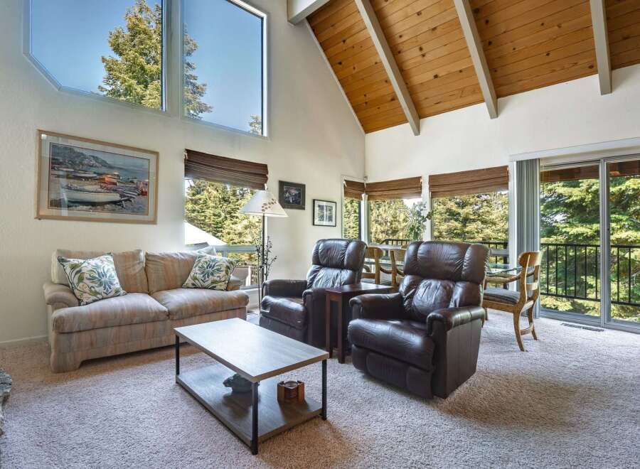 Experience breathtaking views from this stunning living room, featuring a grand vaulted ceiling with exposed wood beams and expansive windows that flood the space with natural light.