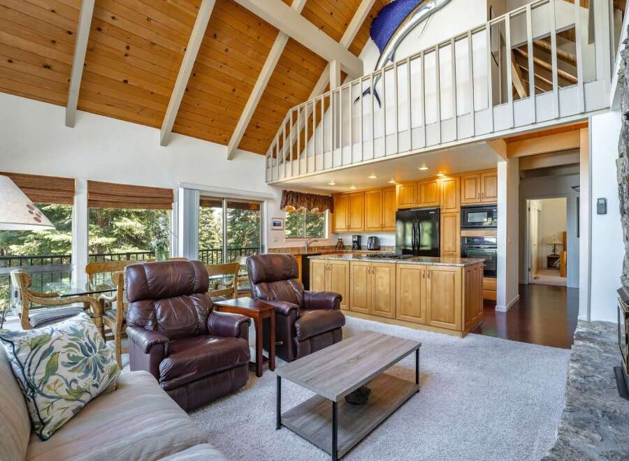 Experience rustic charm and modern comfort in this spacious living area, featuring a vaulted wood-beamed ceiling and a cozy stone fireplace.