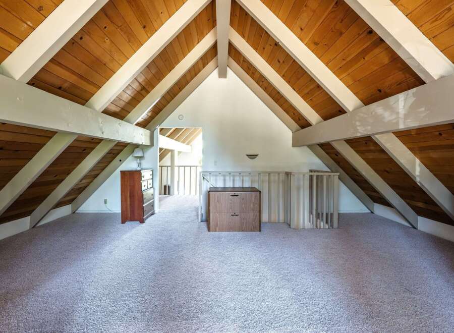 Discover this charming attic space featuring a vaulted wood-paneled ceiling with exposed beams, creating a warm and inviting atmosphere.