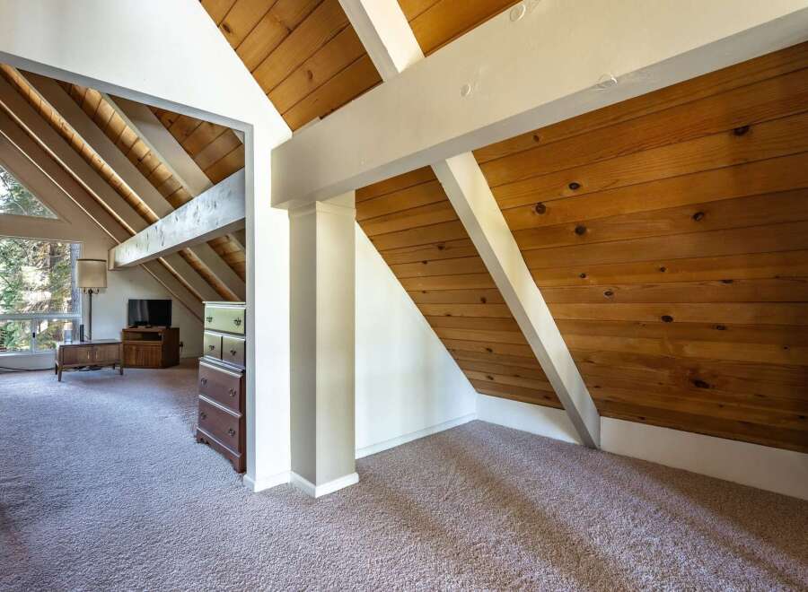 Discover a charming attic space with a unique A-frame design, featuring exposed wooden beams and paneled walls that add rustic warmth.