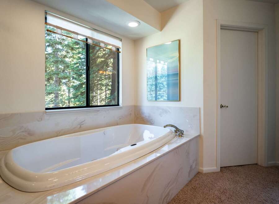 Indulge in relaxation in this luxurious bathroom featuring a spacious soaking tub with a stunning view of the surrounding forest.
