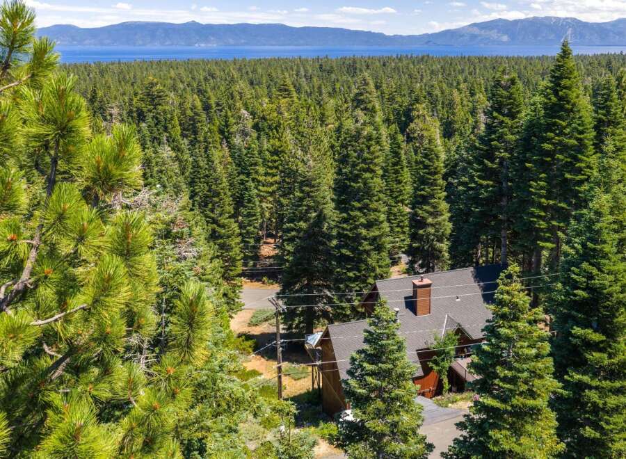 Nestled amidst a dense forest of towering pine trees, this charming home offers a serene retreat with breathtaking views of a distant lake and mountains.
