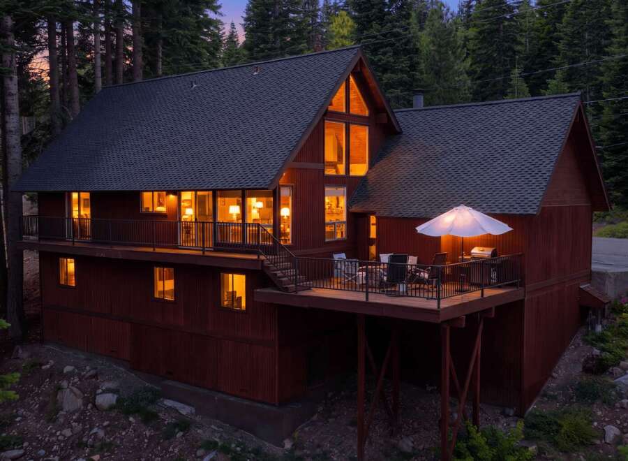 Nestled amidst towering trees, this charming red cabin offers a cozy retreat with its warm interior lights glowing invitingly.