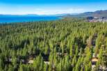 Experience the ultimate lakeside living with this stunning aerial view of a property nestled amidst a lush pine forest, offering breathtaking vistas of a crystal-clear blue lake and distant mountains.