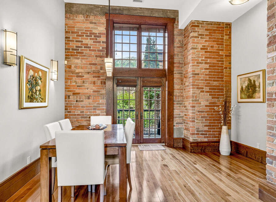 Experience industrial-chic living in this stunning dining area, featuring exposed brick walls and a grand wooden-framed window that floods the space with natural light.