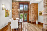 Experience industrial-chic living in this stunning dining area, featuring exposed brick walls and a grand wooden-framed window that floods the space with natural light.