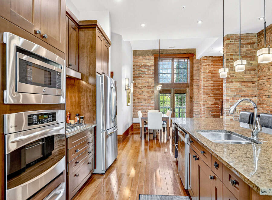 Experience luxury urban living in this stunning loft-style kitchen, featuring sleek stainless steel appliances, rich wood cabinetry, and exposed brick walls.