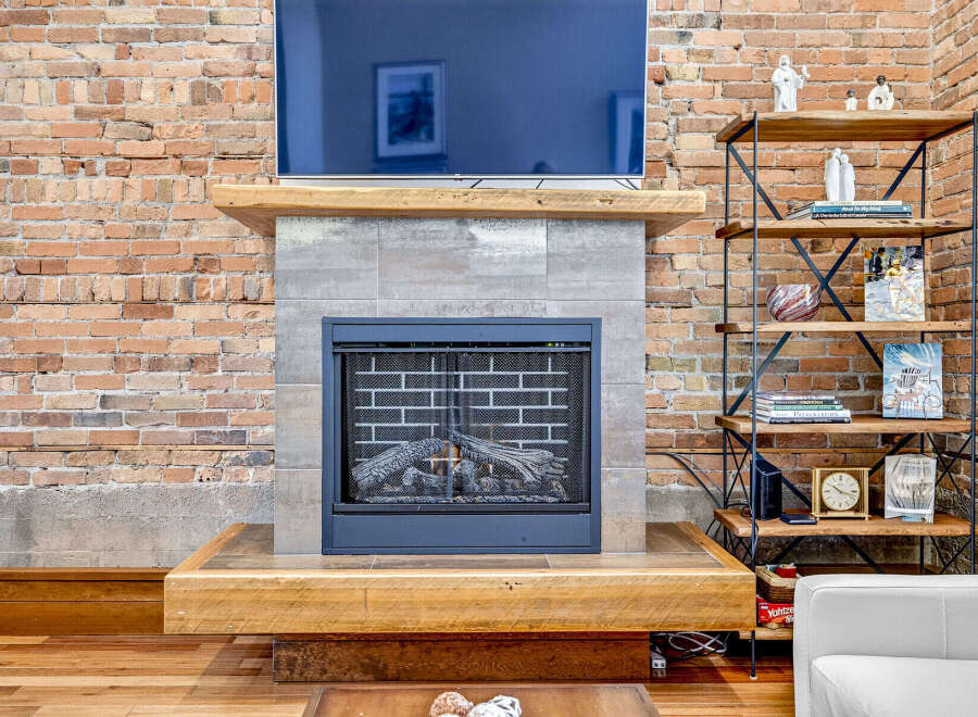 Experience rustic charm with this exposed brick fireplace, featuring a modern gas insert and a thick wooden mantel.