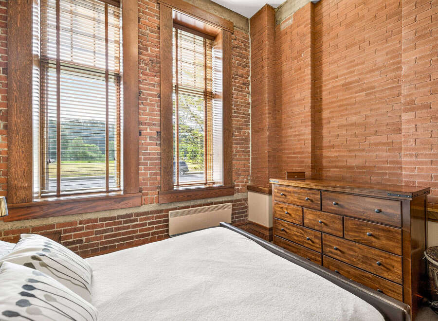 Experience industrial-chic living in this bedroom featuring exposed brick walls and large windows that flood the space with natural light.