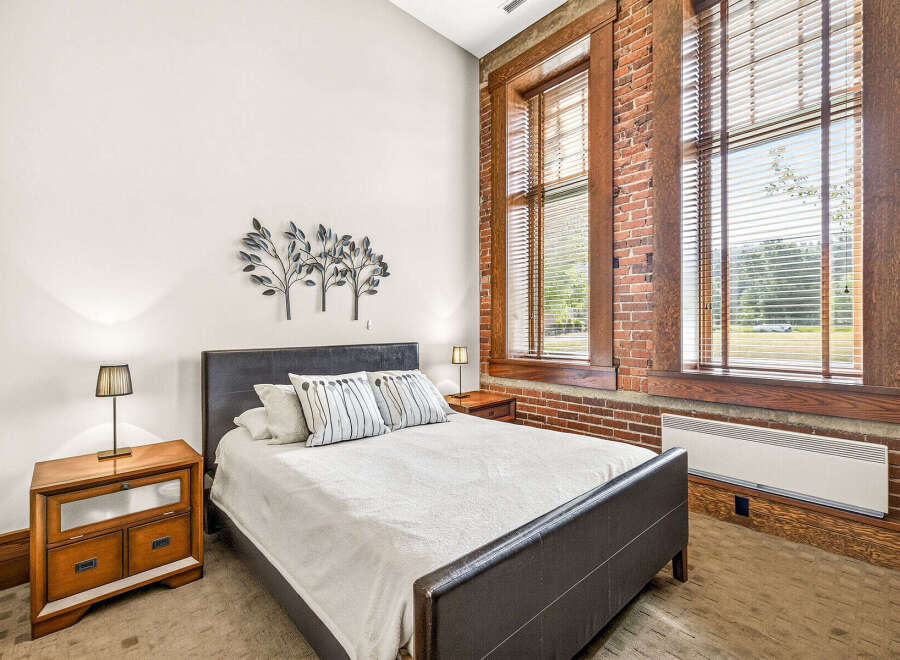 Experience industrial charm in this beautifully appointed bedroom, featuring exposed brick walls and large wooden-framed windows that flood the space with natural light.