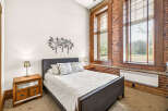 Experience industrial charm in this beautifully appointed bedroom, featuring exposed brick walls and large wooden-framed windows that flood the space with natural light.
