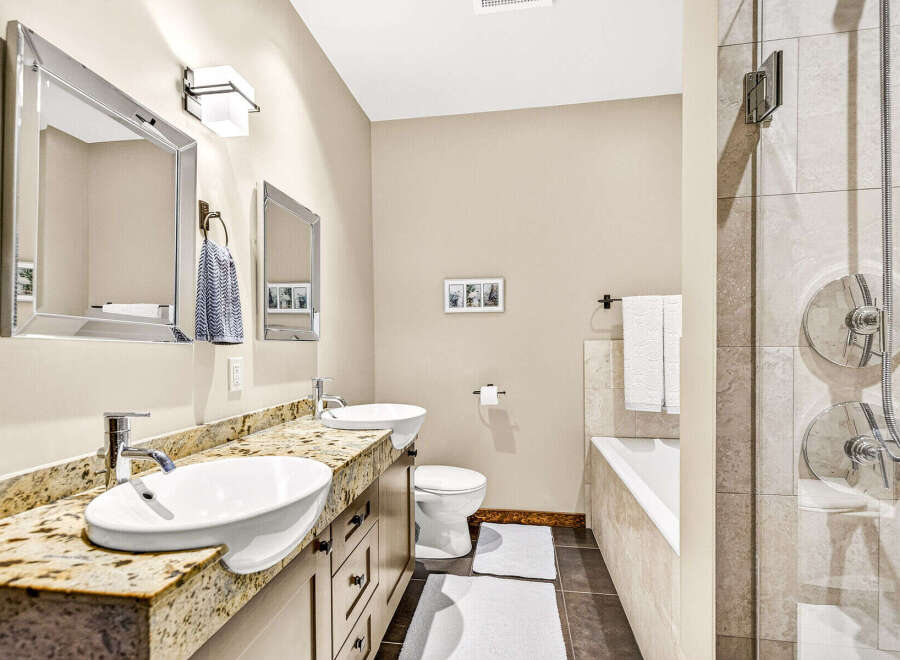 This luxurious bathroom features a spacious double vanity with granite countertops and vessel sinks, complemented by modern chrome fixtures.