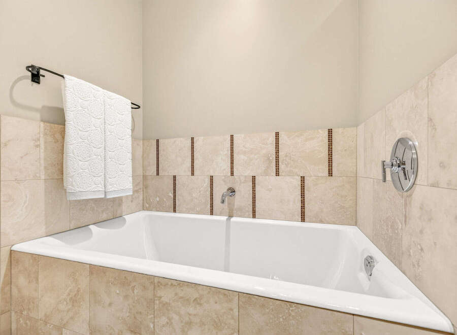 Indulge in relaxation in this luxurious corner bathtub, featuring elegant marble tile surround and a convenient towel rack.