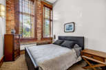 Experience industrial-chic living in this stunning bedroom featuring exposed brick walls and large wooden-framed windows that flood the space with natural light.
