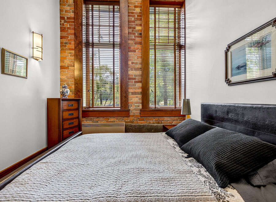 Experience industrial-chic living in this stunning bedroom featuring exposed brick walls and large wooden-framed windows that flood the space with natural light.