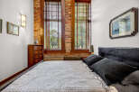 Experience industrial-chic living in this stunning bedroom featuring exposed brick walls and large wooden-framed windows that flood the space with natural light.