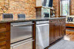 This kitchen island features sleek stainless steel appliances, including a dishwasher and a drawer-style refrigerator, complemented by rich dark wood cabinetry.