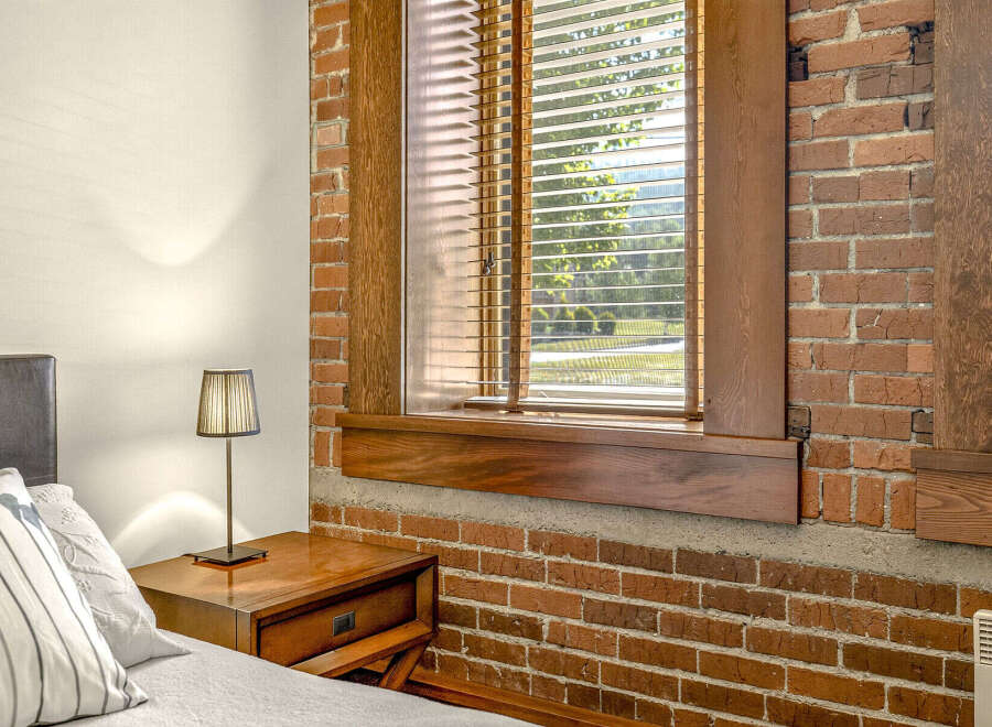 Experience urban living in this charming loft-style bedroom, featuring exposed brick walls and a large window with blinds that let in plenty of natural light.