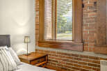 Experience urban living in this charming loft-style bedroom, featuring exposed brick walls and a large window with blinds that let in plenty of natural light.