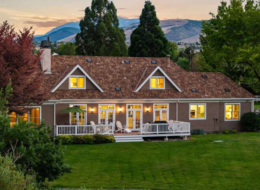 This charming home features a spacious deck overlooking a lush green lawn and scenic mountain views.