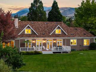 This charming home features a spacious deck overlooking a lush green lawn and scenic mountain views.