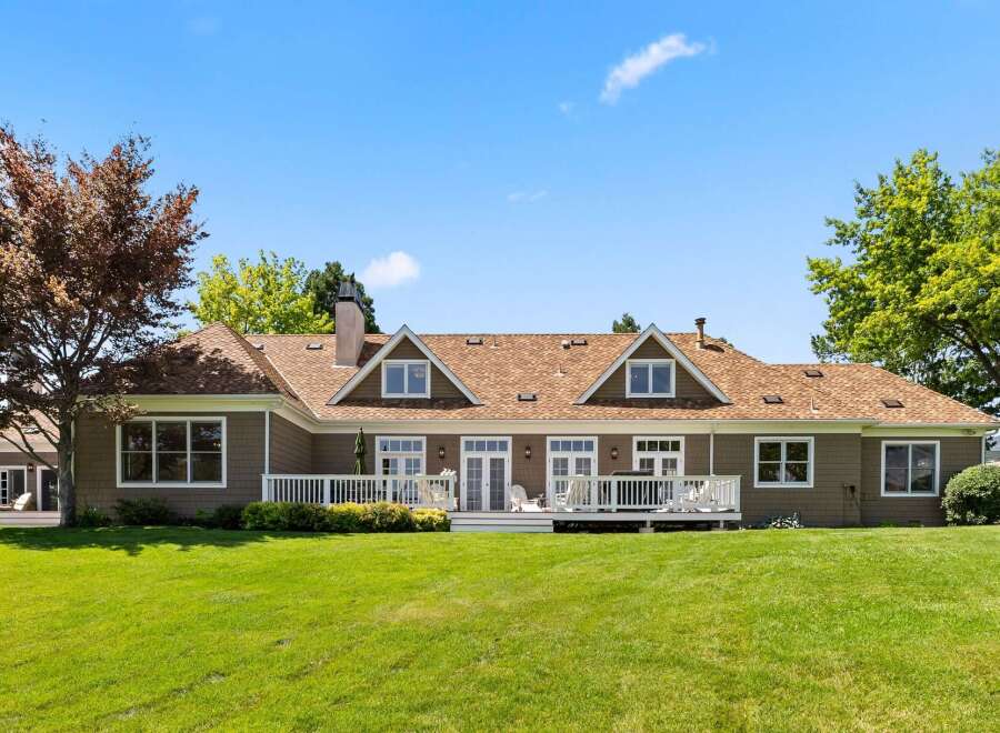 This expansive home features a charming brown exterior with a classic brown shingle roof, complemented by a spacious white deck perfect for outdoor entertaining.