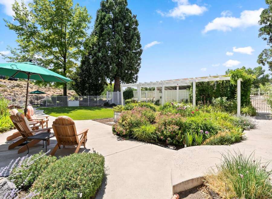 Enjoy outdoor living in this beautifully landscaped backyard featuring comfortable Adirondack chairs under a large green umbrella, perfect for relaxing.