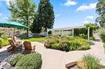Enjoy outdoor living in this beautifully landscaped backyard featuring comfortable Adirondack chairs under a large green umbrella, perfect for relaxing.