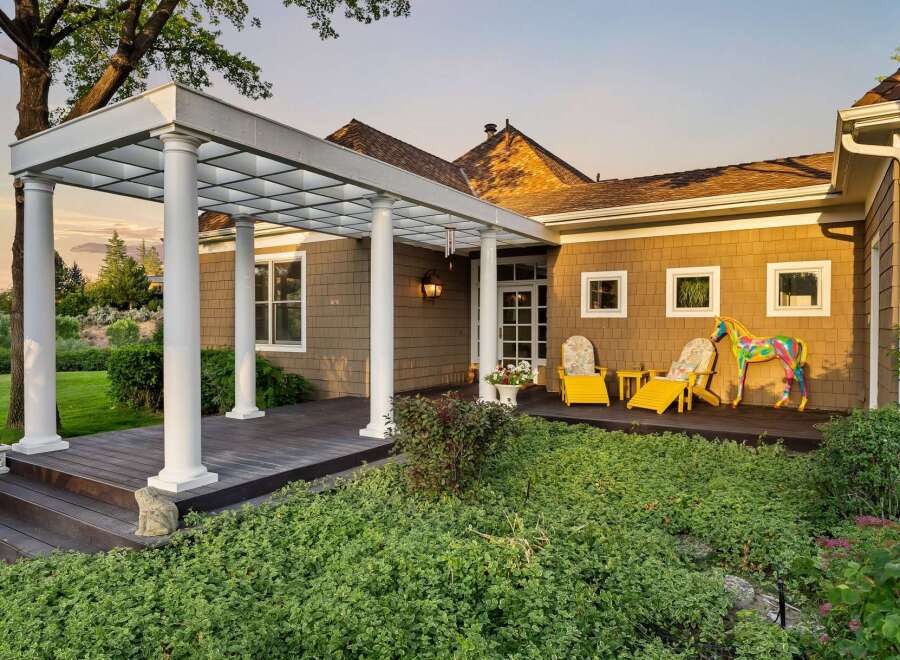 Step onto the expansive wooden deck, partially covered by a charming white pergola supported by elegant columns, offering a perfect spot for outdoor relaxation.