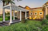 Step onto the expansive wooden deck, partially covered by a charming white pergola supported by elegant columns, offering a perfect spot for outdoor relaxation.