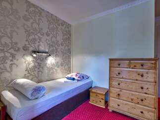 Discover this charming bedroom featuring a comfortable single bed with a decorative pillow and a rolled duvet, perfect for a cozy retreat.