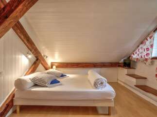 Experience cozy living in this charming attic bedroom, featuring exposed wooden beams and a sloped ceiling for a unique architectural feel.