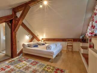 Discover this charming attic bedroom featuring exposed wooden beams and a cozy white bed with striped pillows.