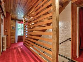 Experience rustic charm in this wood-paneled interior featuring a vibrant red carpeted hallway leading to a staircase with a unique slatted wooden divider.