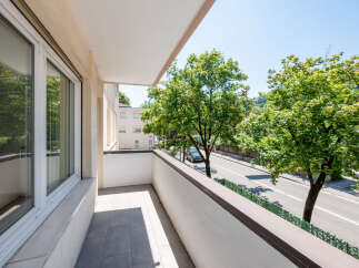 Enjoy the outdoors from this charming balcony, offering a serene view of lush green trees and a quiet street.