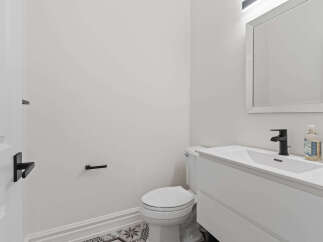This modern bathroom features a sleek white vanity with a minimalist black faucet, complemented by a matching toilet and a decorative tiled floor.