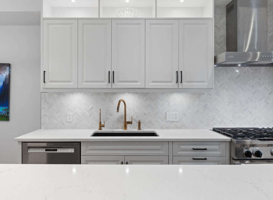 Experience modern luxury in this stunning kitchen, featuring sleek white cabinetry and a beautiful herringbone tile backsplash.