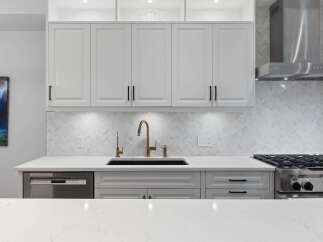 Experience modern luxury in this stunning kitchen, featuring sleek white cabinetry and a beautiful herringbone tile backsplash.