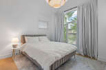 Experience comfort and style in this beautifully appointed bedroom, featuring a plush upholstered bed and a large arched window that floods the space with natural light.