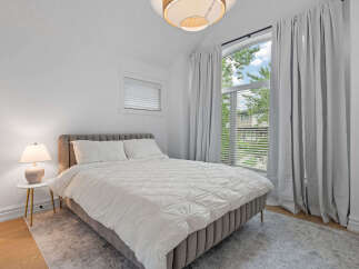 Experience comfort and style in this beautifully appointed bedroom, featuring a plush upholstered bed and a large arched window that floods the space with natural light.