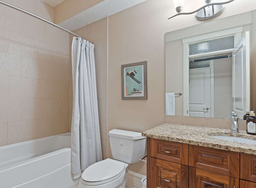 This bathroom features a spacious bathtub with a white shower curtain, a modern toilet, and a vanity with a granite countertop.