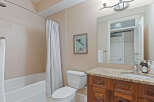 This bathroom features a spacious bathtub with a white shower curtain, a modern toilet, and a vanity with a granite countertop.