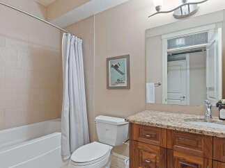 This bathroom features a spacious bathtub with a white shower curtain, a modern toilet, and a vanity with a granite countertop.