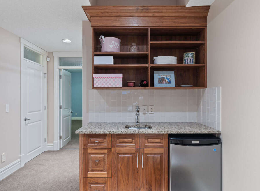 Discover this charming wet bar, perfect for entertaining, featuring a sleek stainless steel mini-fridge and ample storage in the rich wood cabinetry.